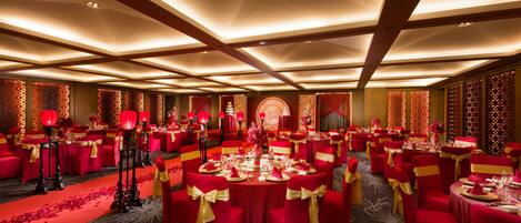 A banquet hall with round tables, red chairs, and a carpeted floor.