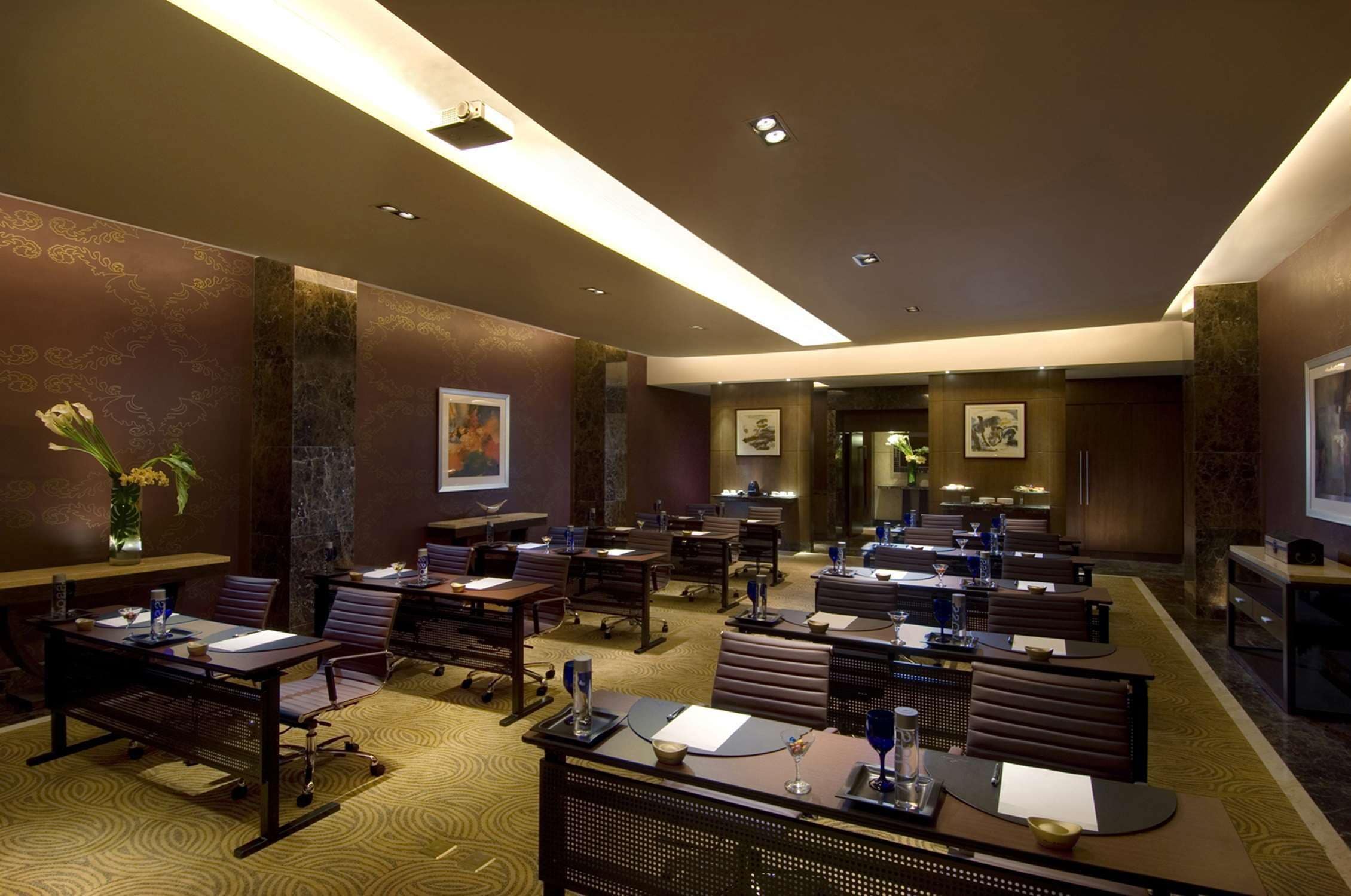 A conference room with multiple tables and chairs, equipped with laptops and presentation screens.