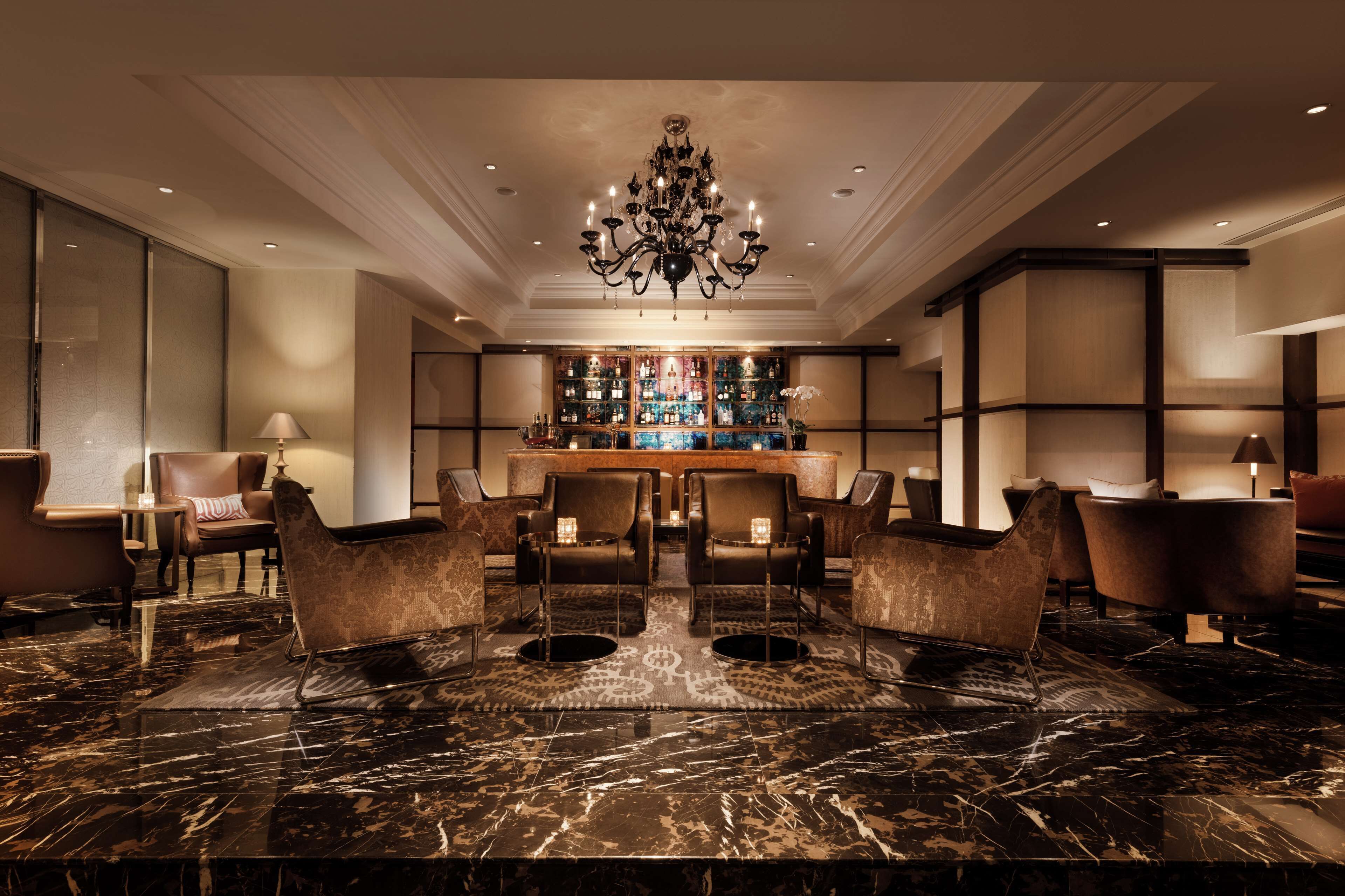 A luxurious lobby with a marble reception desk, leather armchairs, and a chandelier.