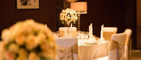 Une table de banquet dressée avec des nappes blanches, des chaises et un centre de table composé de fleurs blanches.