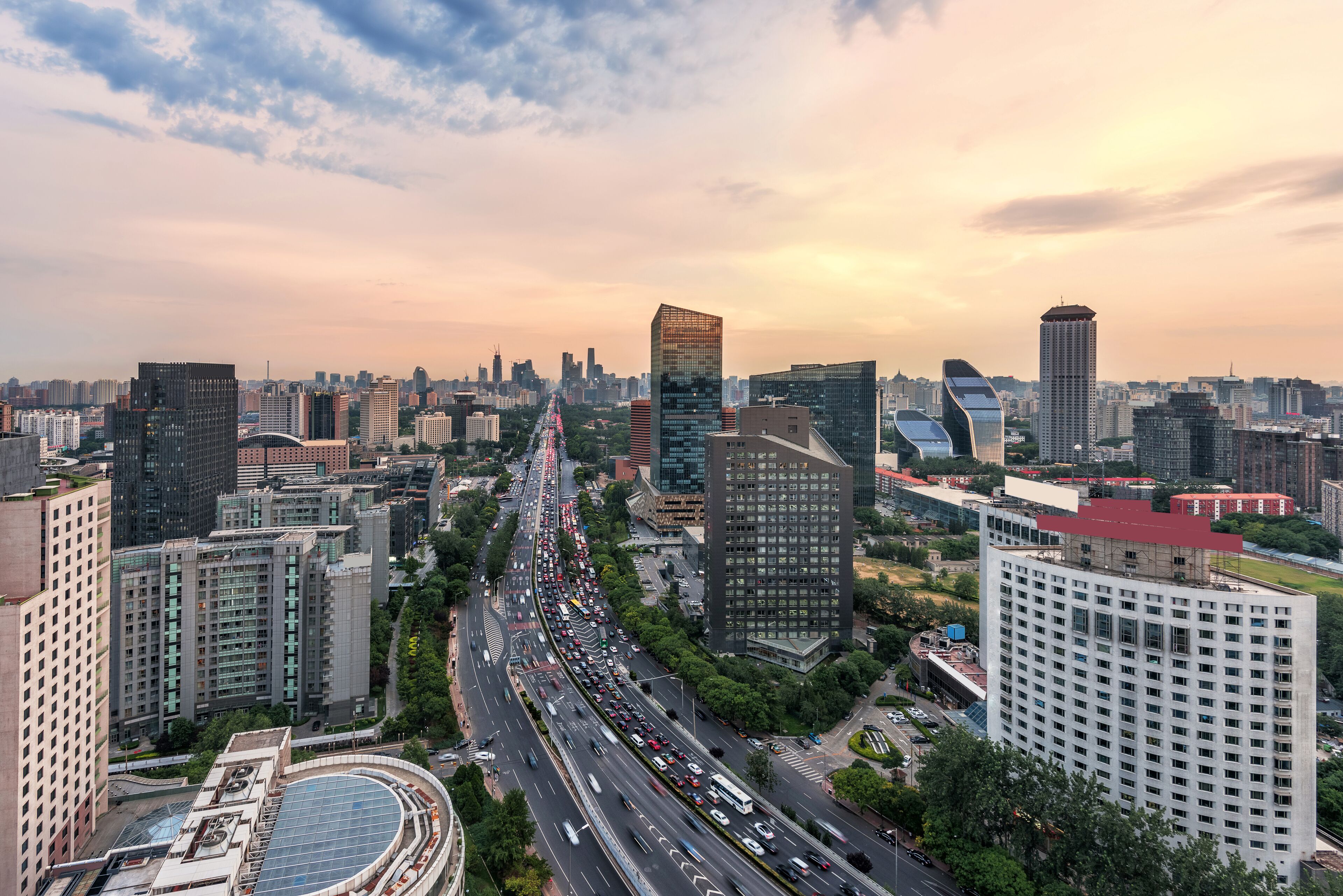 A cityscape with modern high-rise buildings, a busy multi-lane road, and a curved road leading into the city.