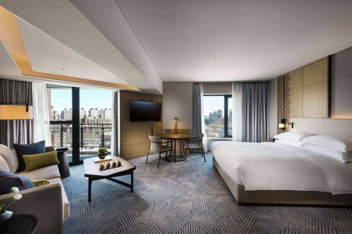 Una habitación de hotel con una cama grande, un sofá, una mesa de comedor y una televisión.