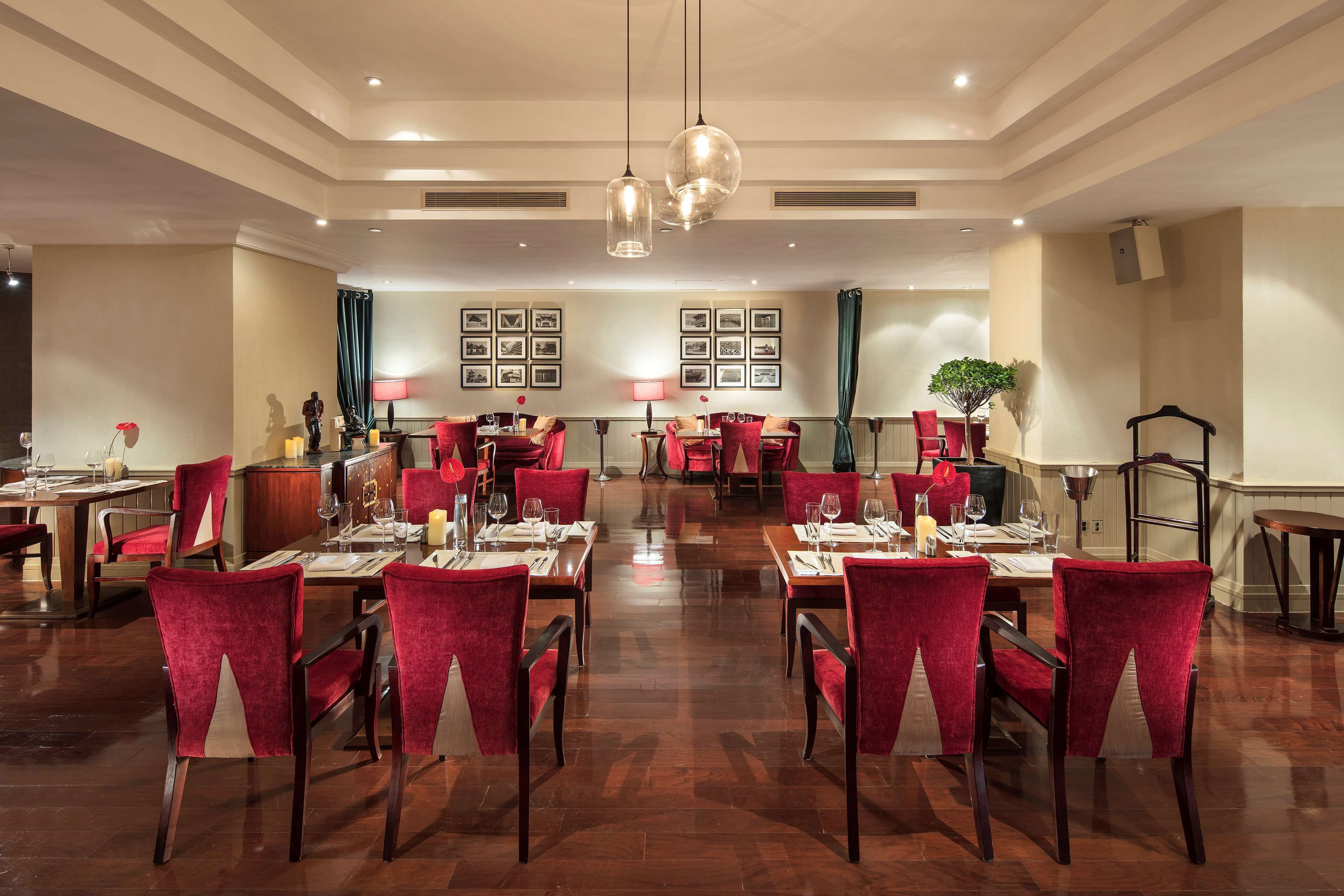 A spacious dining area with red upholstered chairs and tables, set against a backdrop of framed pictures and a chandelier.