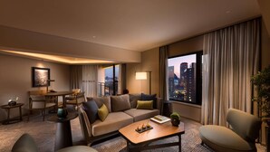 Une chambre d’hôtel moderne, dotée d’un canapé, de fauteuils, d’une table basse et offrant une vue sur la ville.