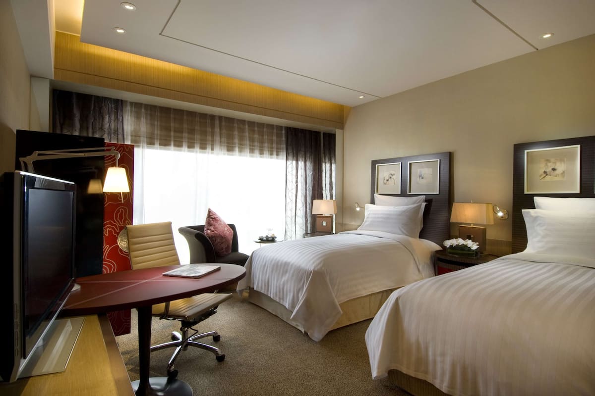 Habitación de hotel con dos camas, un escritorio, un televisor y una ventana con cortinas.