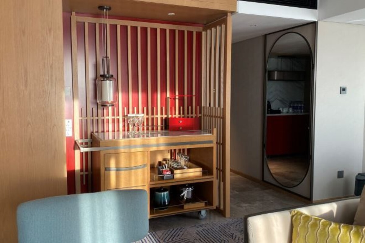 Una habitación de hotel moderna con un separador de madera, un aparador de vidrio y una maleta roja.