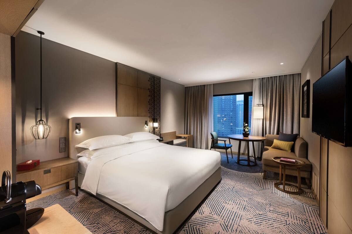 Una habitación de hotel moderna con una cama grande, mesitas de noche, un escritorio con silla, televisión y vista a la ciudad.