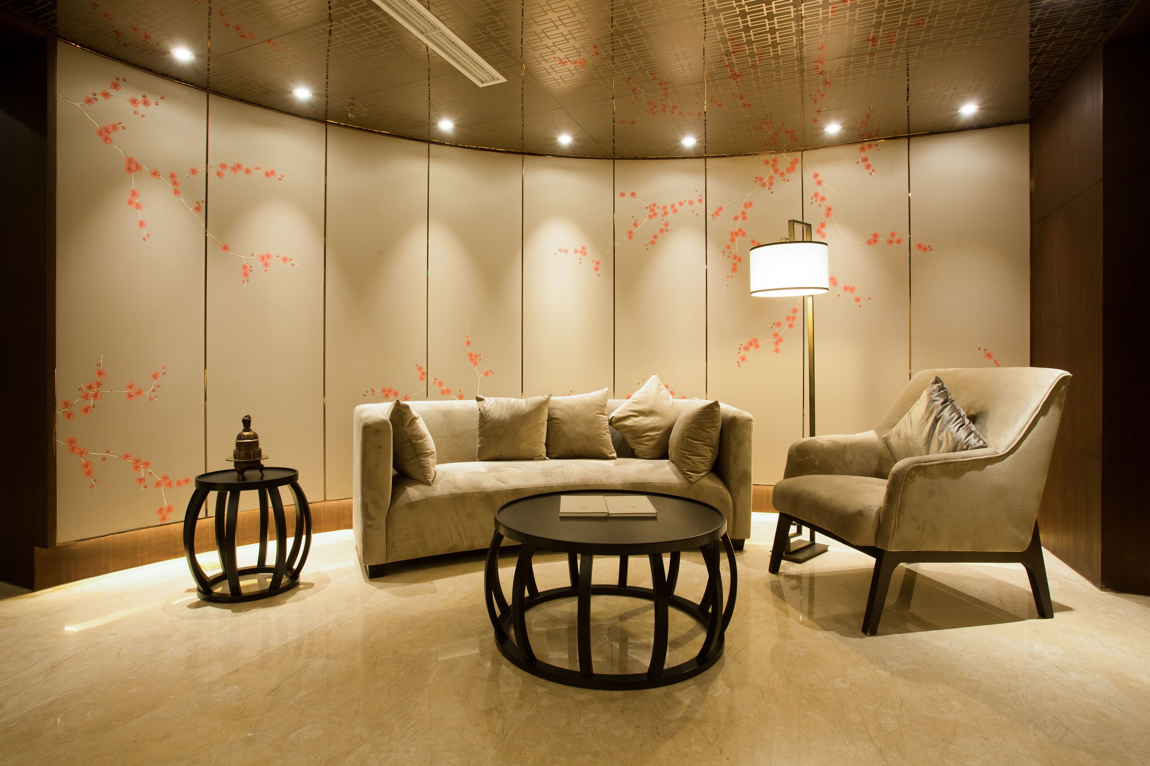 A modern room with a sofa, armchair, and round tables, featuring a decorative wall and a floor lamp.