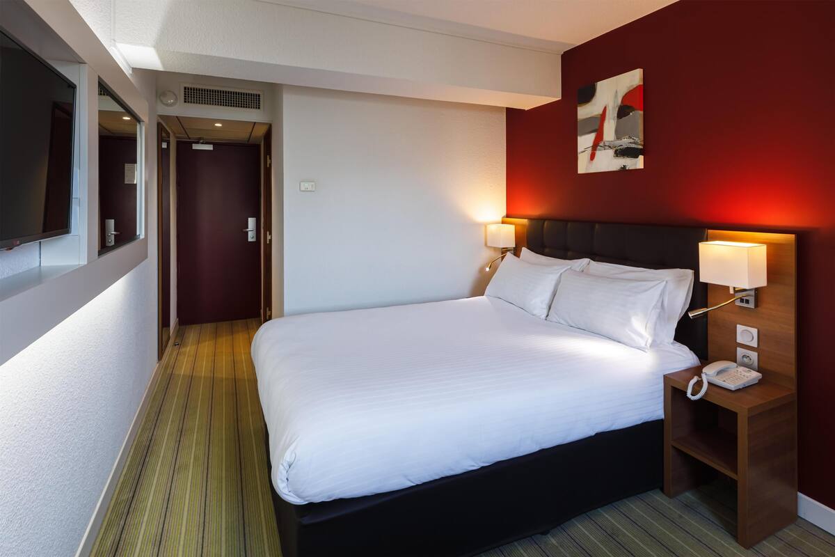 A hotel room with a bed, bedside lamps, a phone, and a painting on the wall.