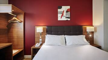 Una habitación de hotel con una cama grande, dos lámparas de noche, una mesita de noche de madera, un teléfono y una pared de acento roja.