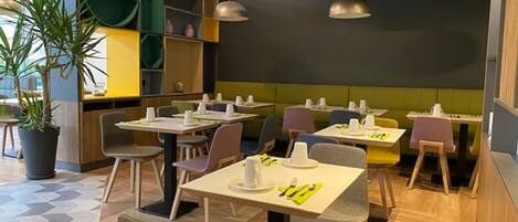 Un restaurante moderno con suelo de patrón hexagonal, zonas de estar en tonos verde y amarillo, y plantas en macetas.