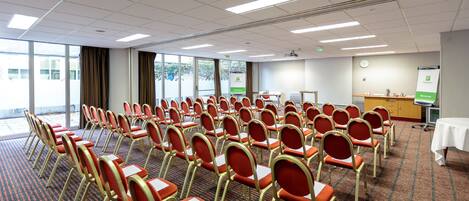 A conference room with rows of red and gold chairs, a projector screen, and a whiteboard.