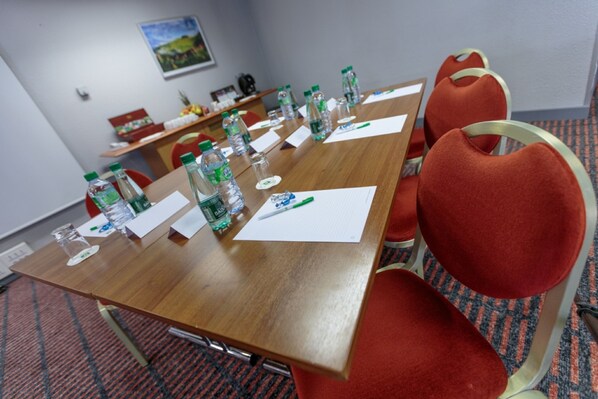 Un salón de conferencias con una mesa de madera, sillas rojas, botellas de agua y documentos.