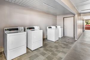 A laundry area with three white front-loading washers and dryers, a door to the right, and a tiled floor.