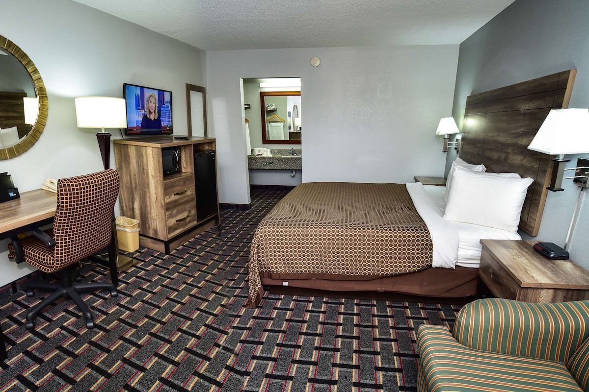 A hotel room with a bed, a desk, a chair, a dresser, a mirror, and a television.