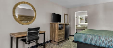 Una habitación de hotel con escritorio, silla, televisor, armario y cama.