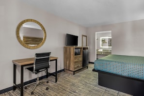 A hotel room with a desk, chair, television, wardrobe, and a bed.