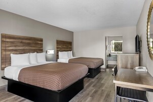 A hotel room with two beds, a desk, a mirror, and a bathroom visible through an open door.