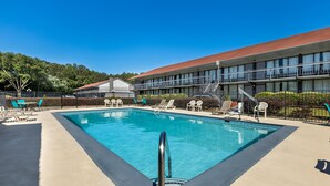 A swimming pool with lounge chairs and a building with a red roof in the background. - Americas Best Value Inn Douglasville (Douglasville)