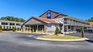 A hotel with a stone facade, a parking lot, and a clear blue sky. - Americas Best Value Inn Douglasville (Douglasville)