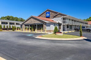 A hotel with a stone facade, a parking lot, and a clear blue sky.