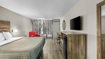 A hotel room with a bed, a red chair, a desk with a flat-screen TV, and a mirror.
