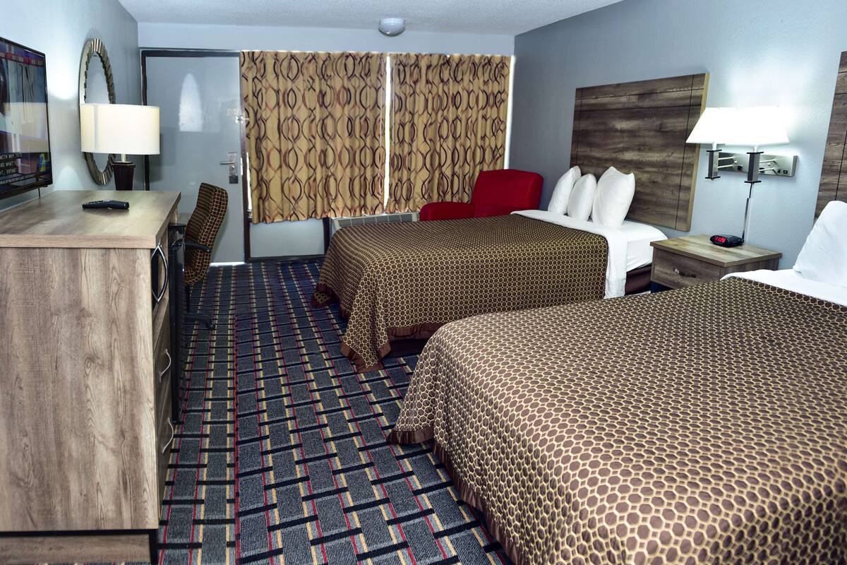A hotel room with two beds, a desk, a chair, a TV, and a patterned carpet.