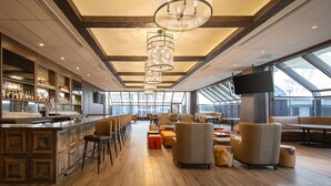A spacious bar area with a long counter, multiple seating options including bar stools and cushioned chairs, and a large window providing natural light. - DoubleTree by Hilton Sacramento (Sacramento)