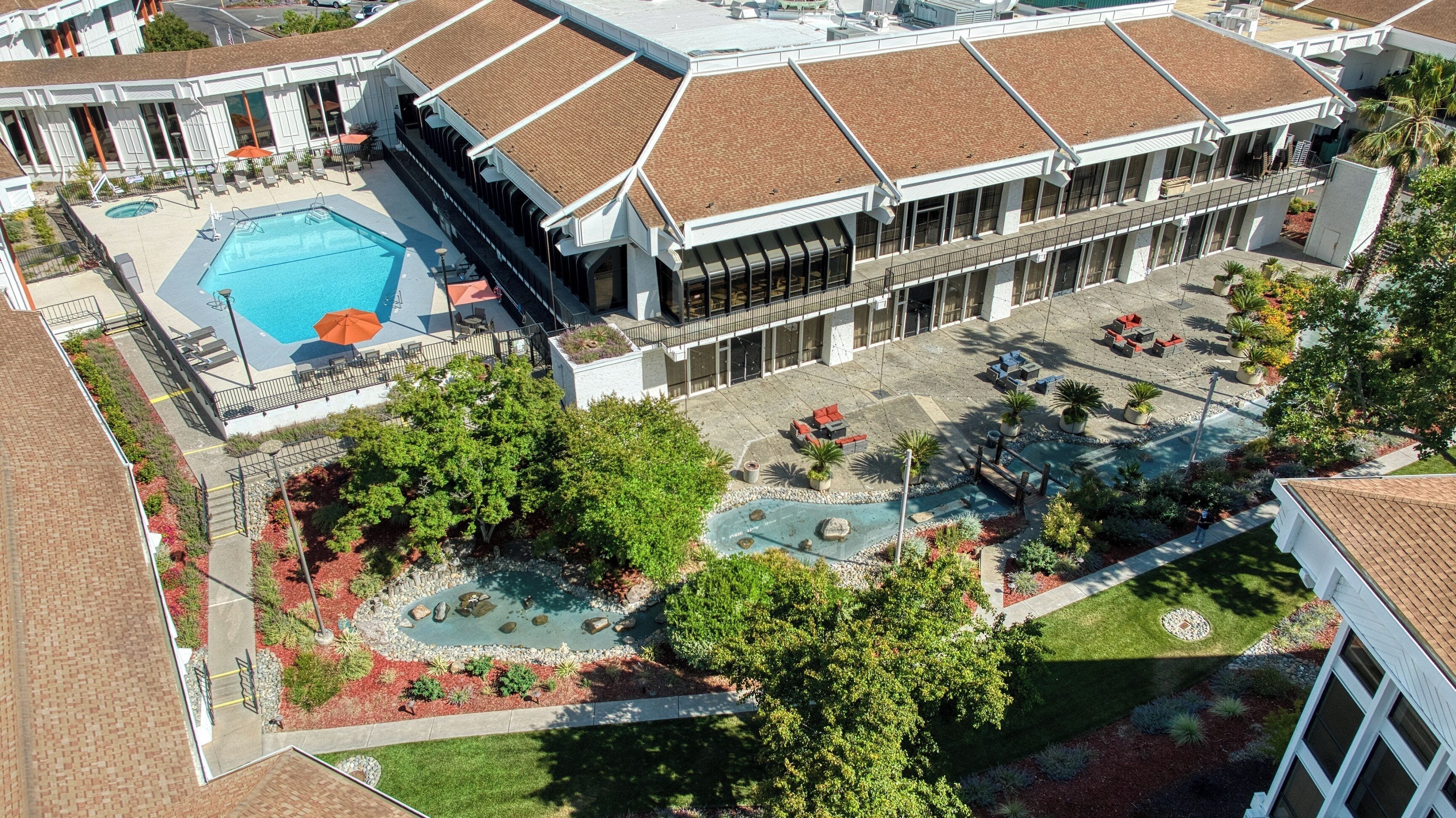 An aerial view of a hotel with a swimming pool, outdoor seating, and landscaped gardens.
