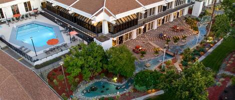 An aerial view of a hotel with a swimming pool, outdoor seating area, and landscaped gardens.