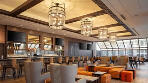A modern bar area with seating, a bar counter with bottles, and large windows. - DoubleTree by Hilton Sacramento (Sacramento)