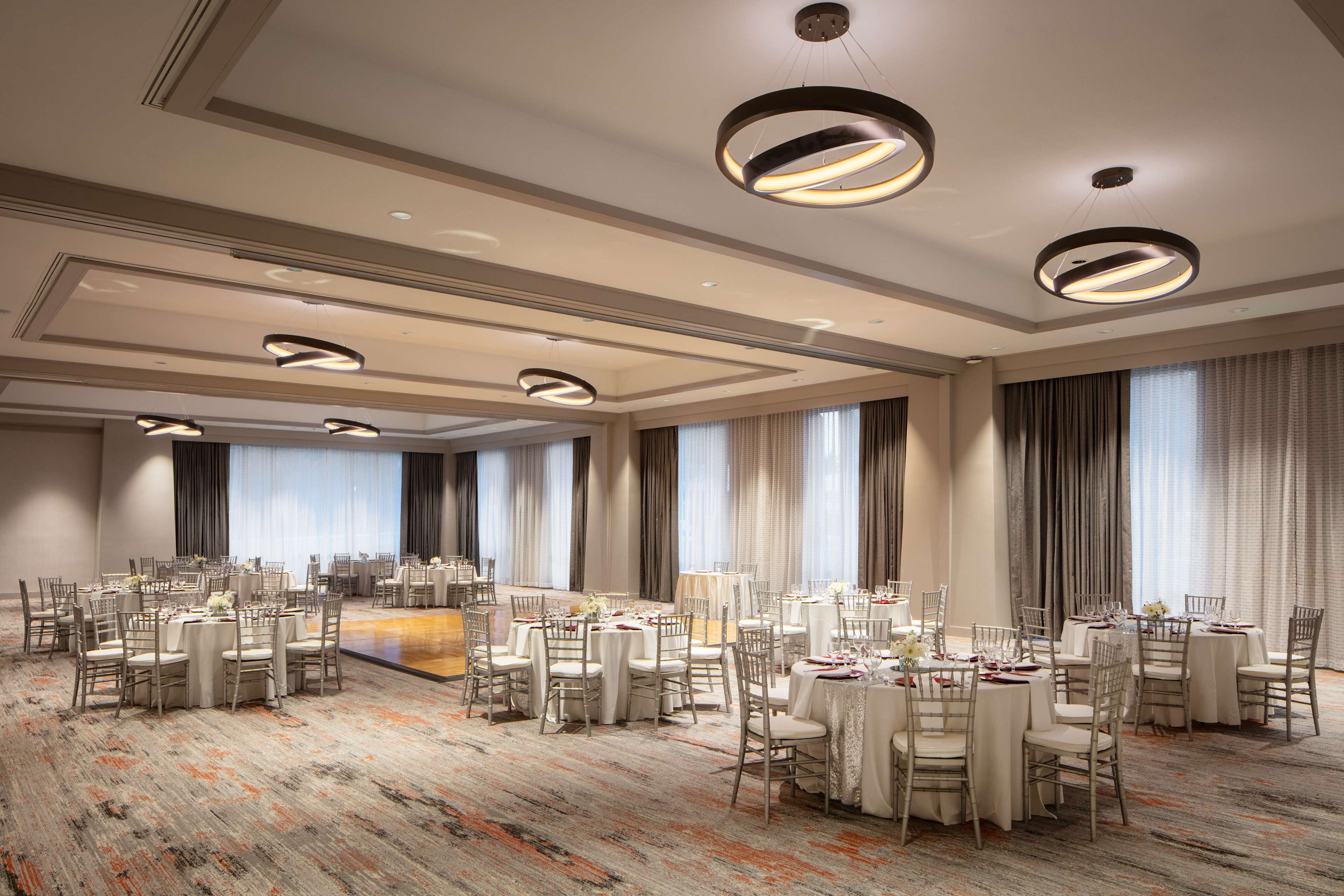 Une salle de banquet spacieuse, dotée de tables et de chaises rondes, de grandes fenêtres et d’un éclairage moderne.
