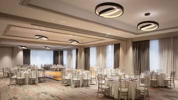 Une salle de banquet spacieuse, dotée de tables et de chaises rondes, de grandes fenêtres et d’un éclairage moderne.