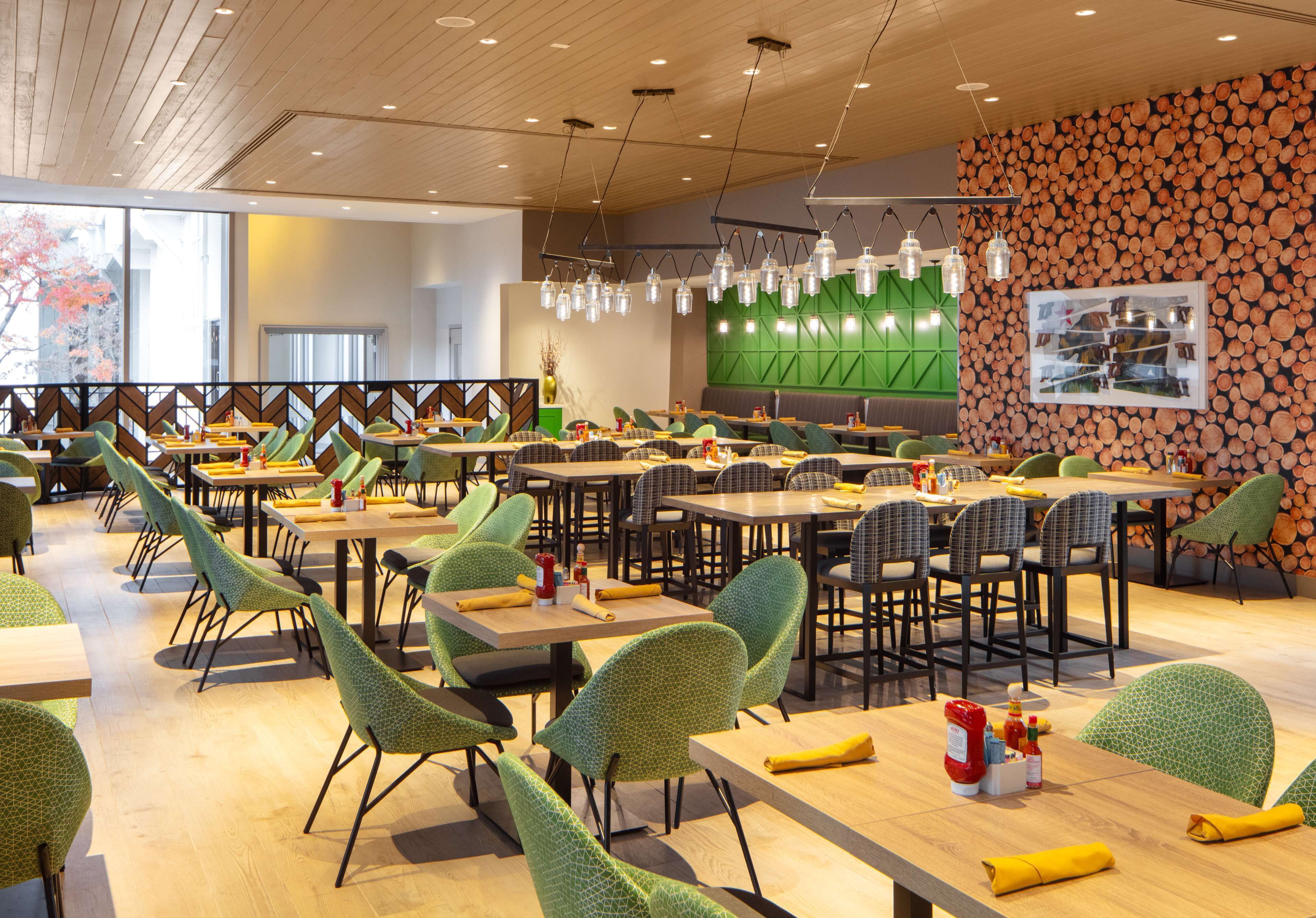 A modern dining area with green patterned chairs, wooden tables, and a green accent wall.