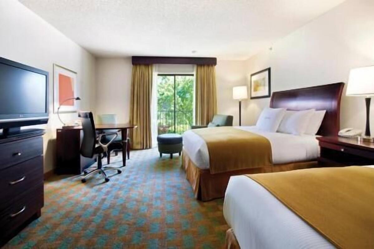 A hotel room with a bed, a desk, a chair, a television, and a window with curtains.