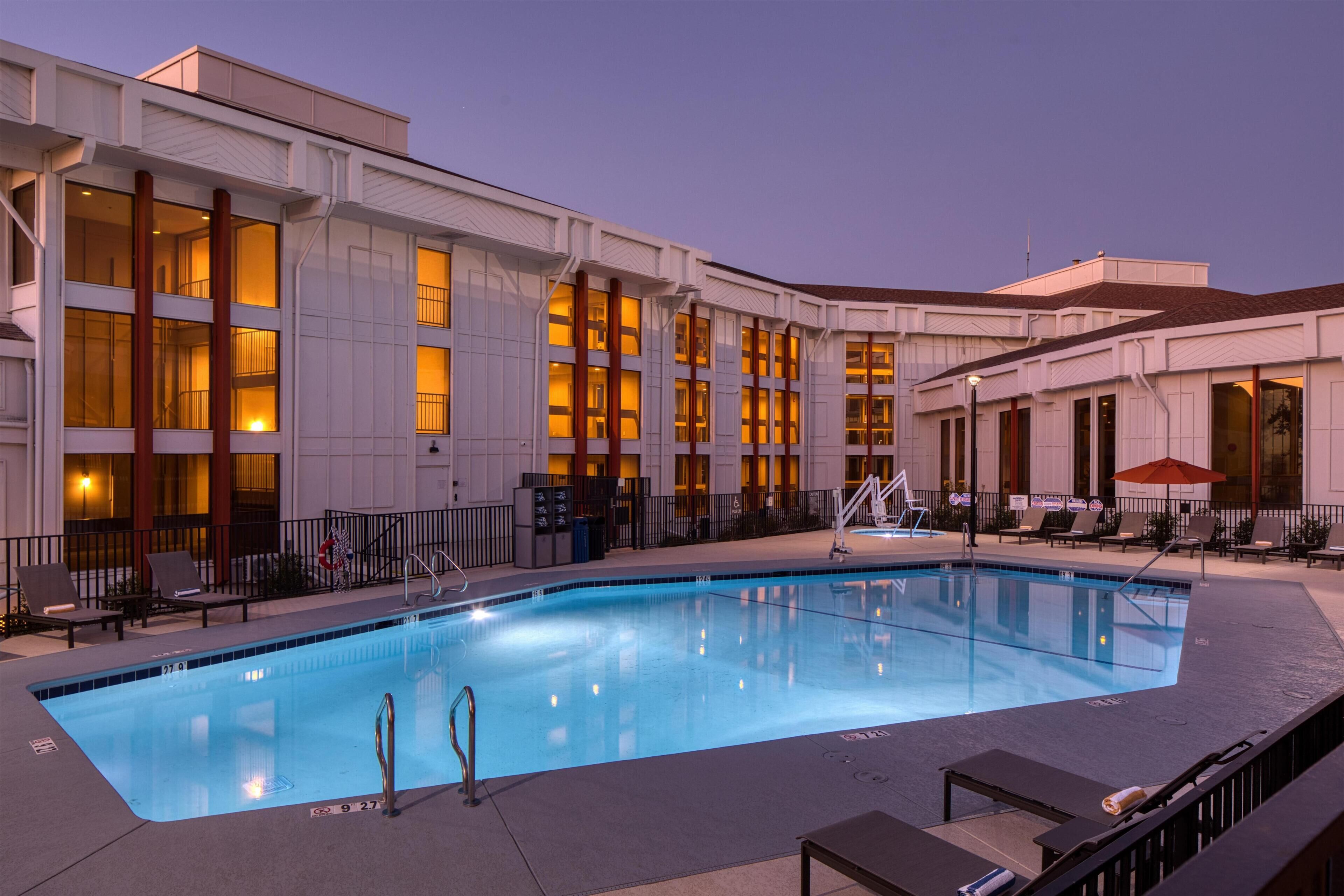 A swimming pool with lounge chairs and a building with large windows.