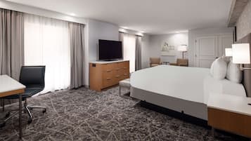 Een hotelkamer met een groot bed, een bureau met stoel, een televisie op een houten dressoir en een lamp op een nachtkastje.