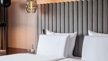 A hotel room with a bed, two pillows, a nightstand, a bottle, and a lamp.