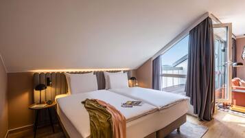 A modern hotel room with a large bed, a side table, a reading lamp, and a view of the outside.