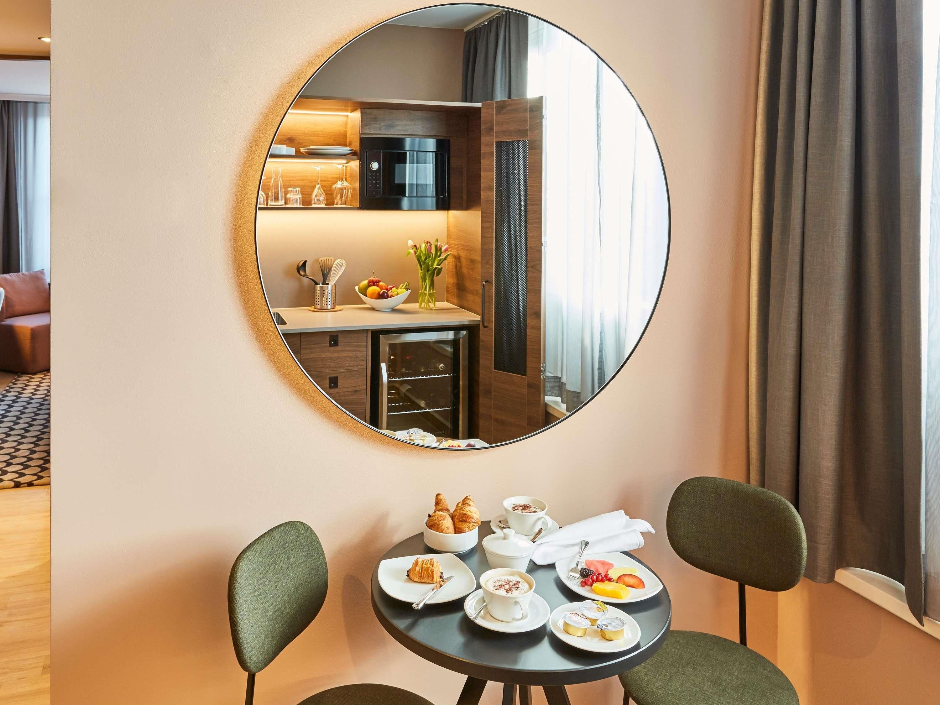 A dining area with a round mirror, a table with plates of food, and a view of a kitchen through the mirror.