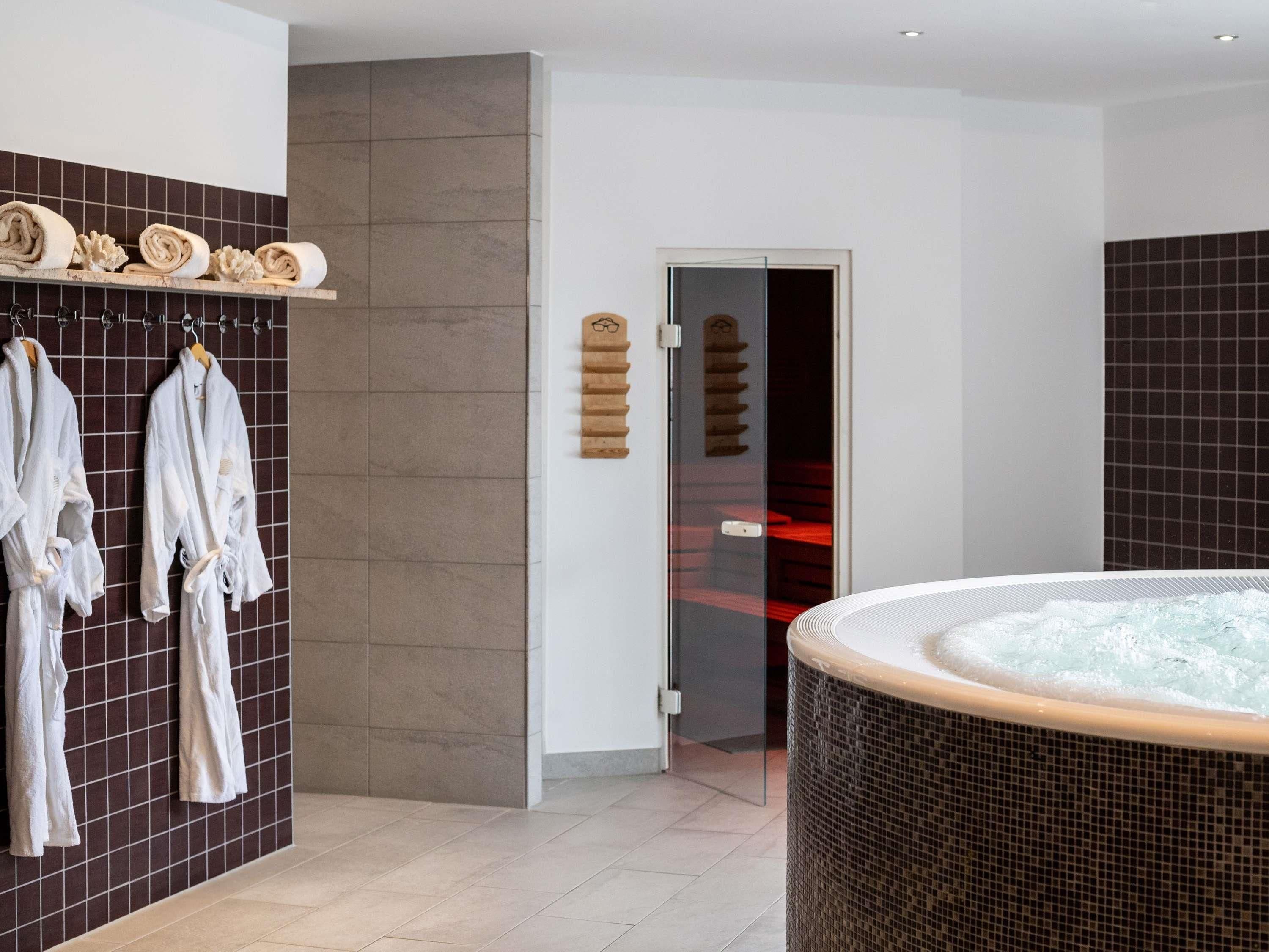 Un baño moderno con bañera de hidromasaje, paredes de azulejos oscuros y un perchero con batas.