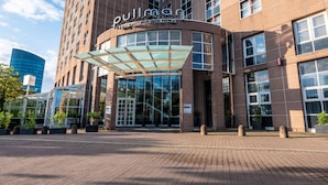 A hotel entrance with a curved glass facade, a prominent sign, and a modern building in the background.
