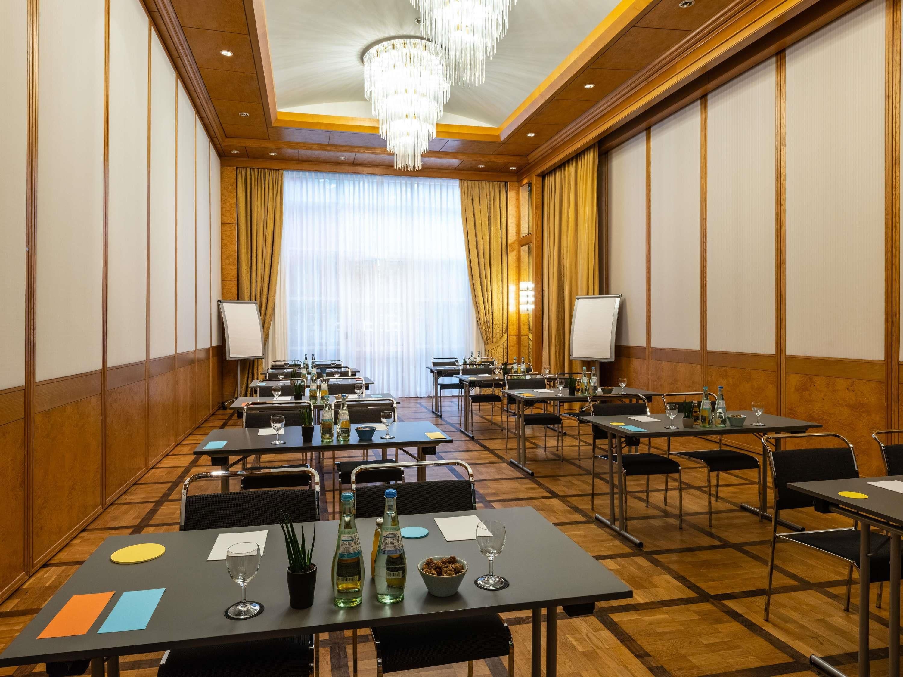 A conference room with tables, chairs, and a large window with curtains.