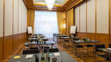 A conference room with tables, chairs, and a large window with curtains.