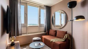 A hotel room with a sofa, a round table, a mirror, a floor lamp, and a TV.