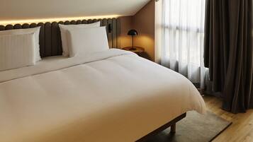 A large bed with a headboard, a bedside table with a lamp, and a window with curtains.