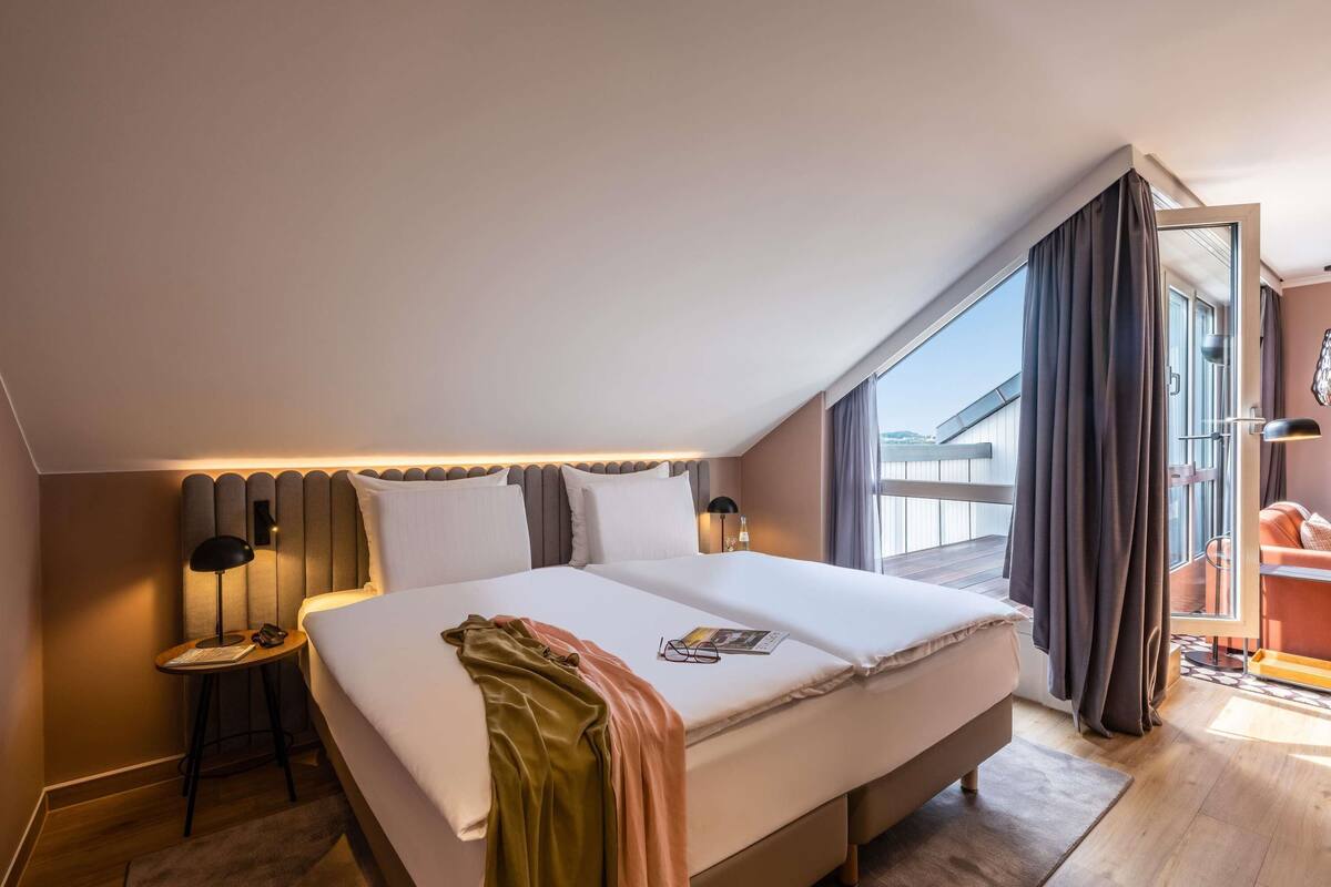 Una habitación de hotel moderna con una cama grande, una mesita auxiliar, una lámpara de lectura y vistas al exterior.