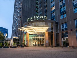 Entrada de un hotel con fachada de vidrio, un toldo curvo y un letrero que dice 'Pullman Hotels'.