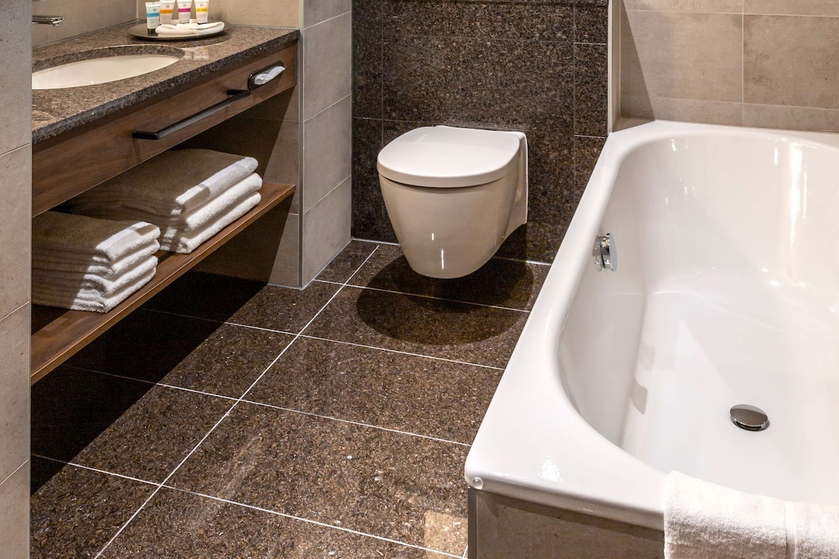 A modern bathroom with a bathtub, a toilet, and a vanity with a sink and towel rack.