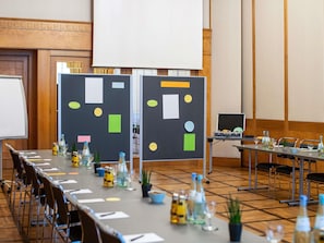 A conference room with a long table, chairs, a projector screen, and a presentation board with various shapes and colors.